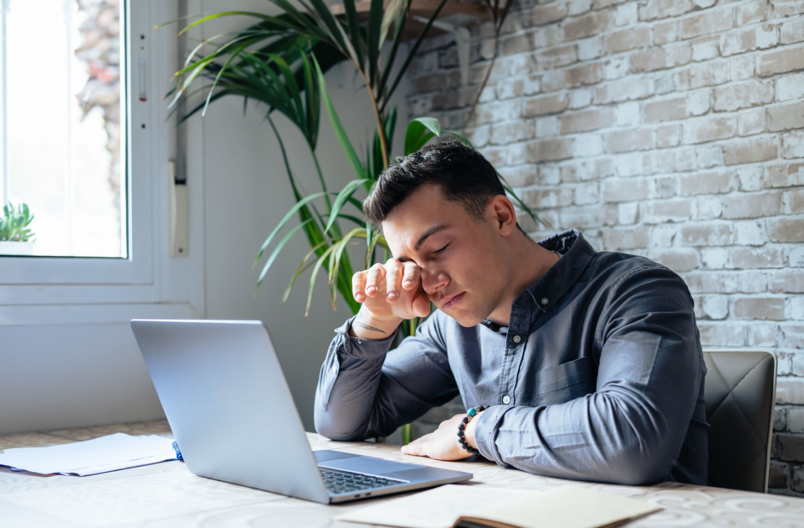 A young adult working at their computer, rubbing their eyes due to digital eye strain.